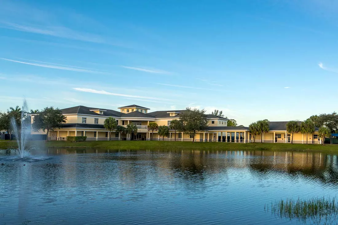 View of the North Broward Preparatory School campus with lake and fountain Lake with fountain with North Broward Preparatory School buildings in the background — American Butler