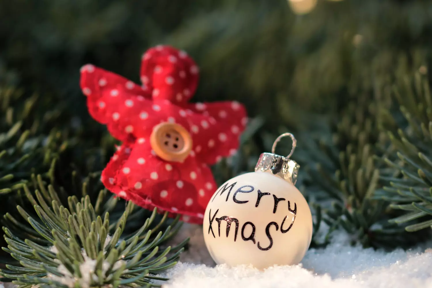 Christmas ornament "Merry Xmas" and angel on a background of fir branches Christmas ornament with the inscription "Merry Xmas" and a red angel figure against a background of green fir branches