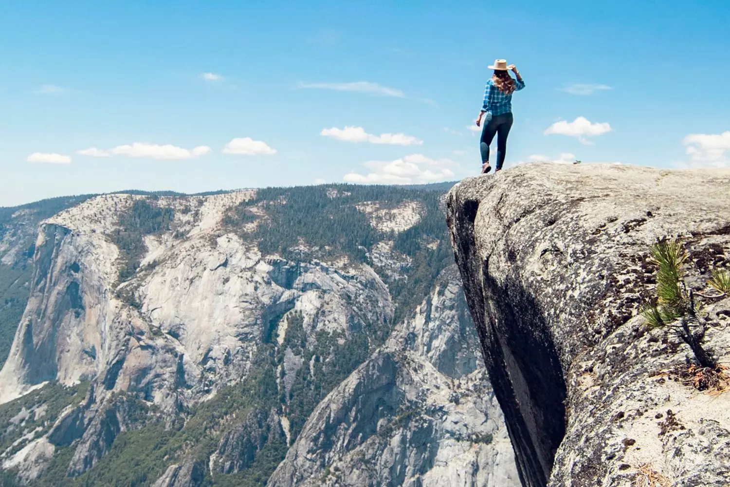 Queen of the Peaks: Conquering Yosemite's Majestic Heights A woman standing triumphantly on a Yosemite mountain summit with vast valley views and dramatic cliffs stretching behind her