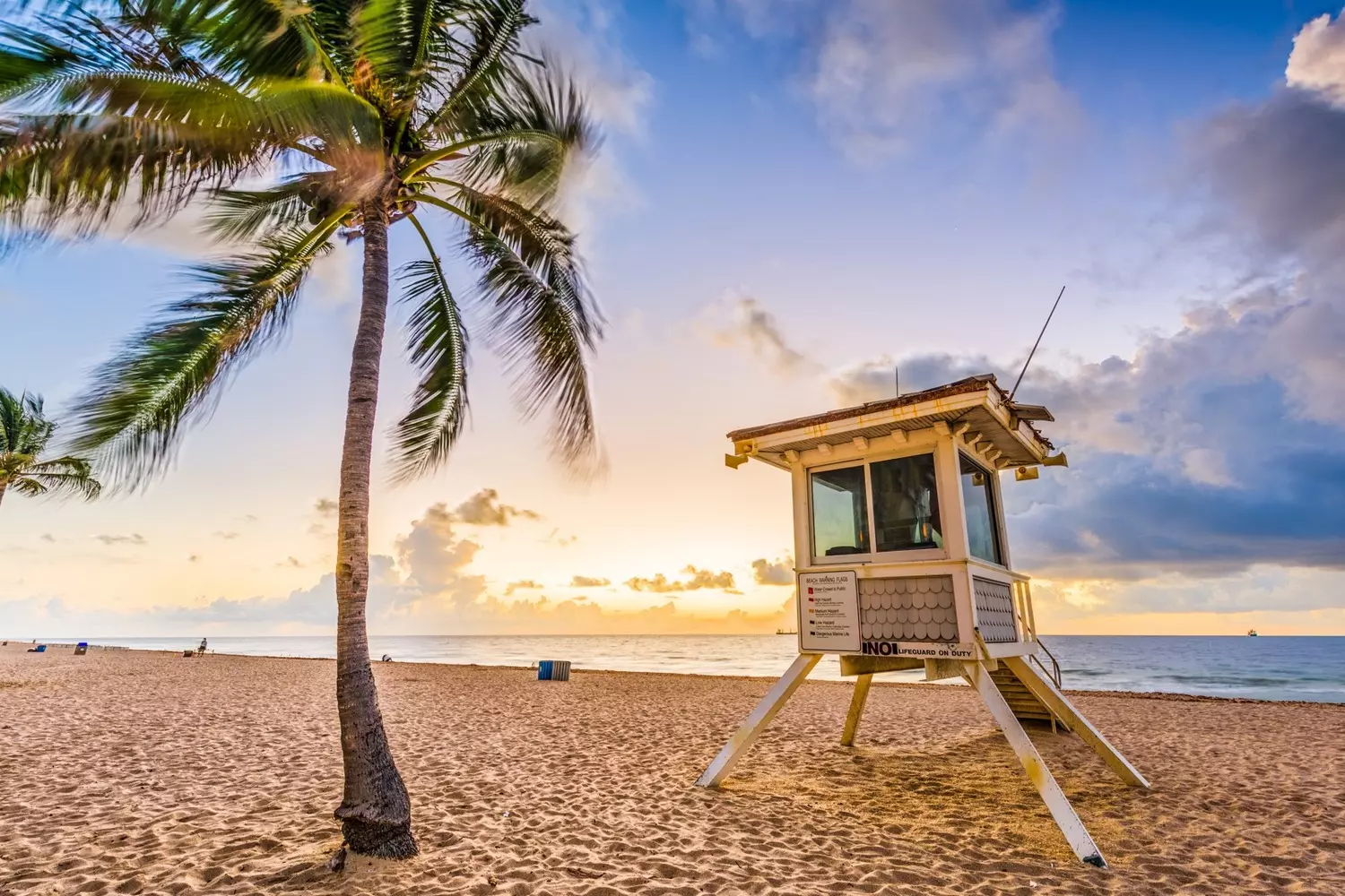 The famous Fort Lauderdale beach: sun, sand, and lifeguard towers A beach with golden sand in Fort Lauderdale, featuring a red-and-white lifeguard tower against the backdrop of the turquoise waters of the Atlantic Ocean, with palm trees and vacationers relaxing under the bright sun