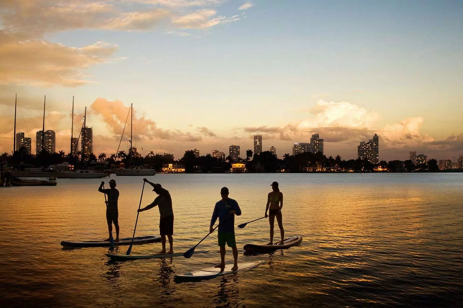 Miami Paddle Board Tours — Sunset Glow Experience Group paddle boarding at golden hour with Miami skyline in background