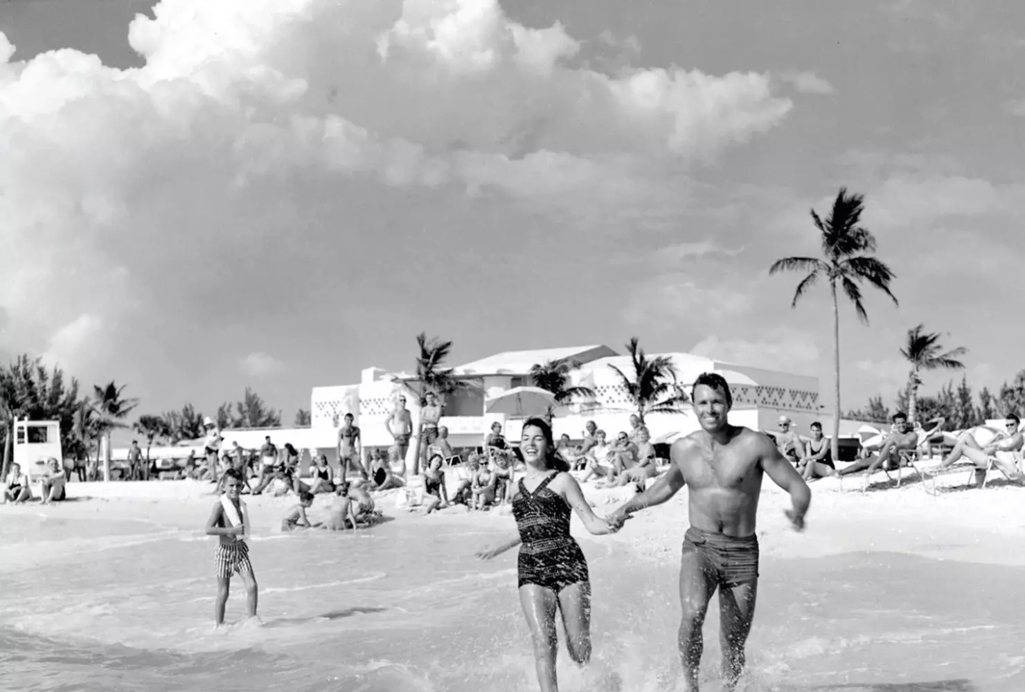 Сарасота в прошлом — ностальгия по пляжам 1950-х Винтажное фото пляжа Сарасота: купальники ретро и старинные автомобили на побережье Флориды