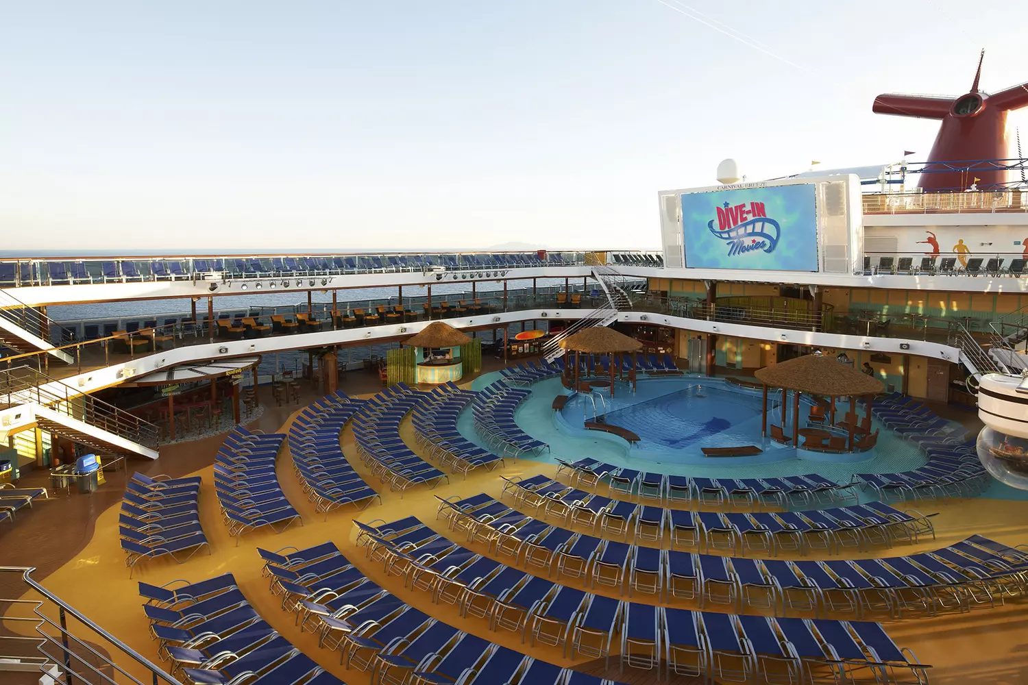 Carnival Breeze Top Deck — Poolside Relaxation with Ocean Views Photo of Carnival Breeze's top deck: two turquoise pools, rows of loungers with blue cushions, a cocktail bar, and sunbathing area under clear skies