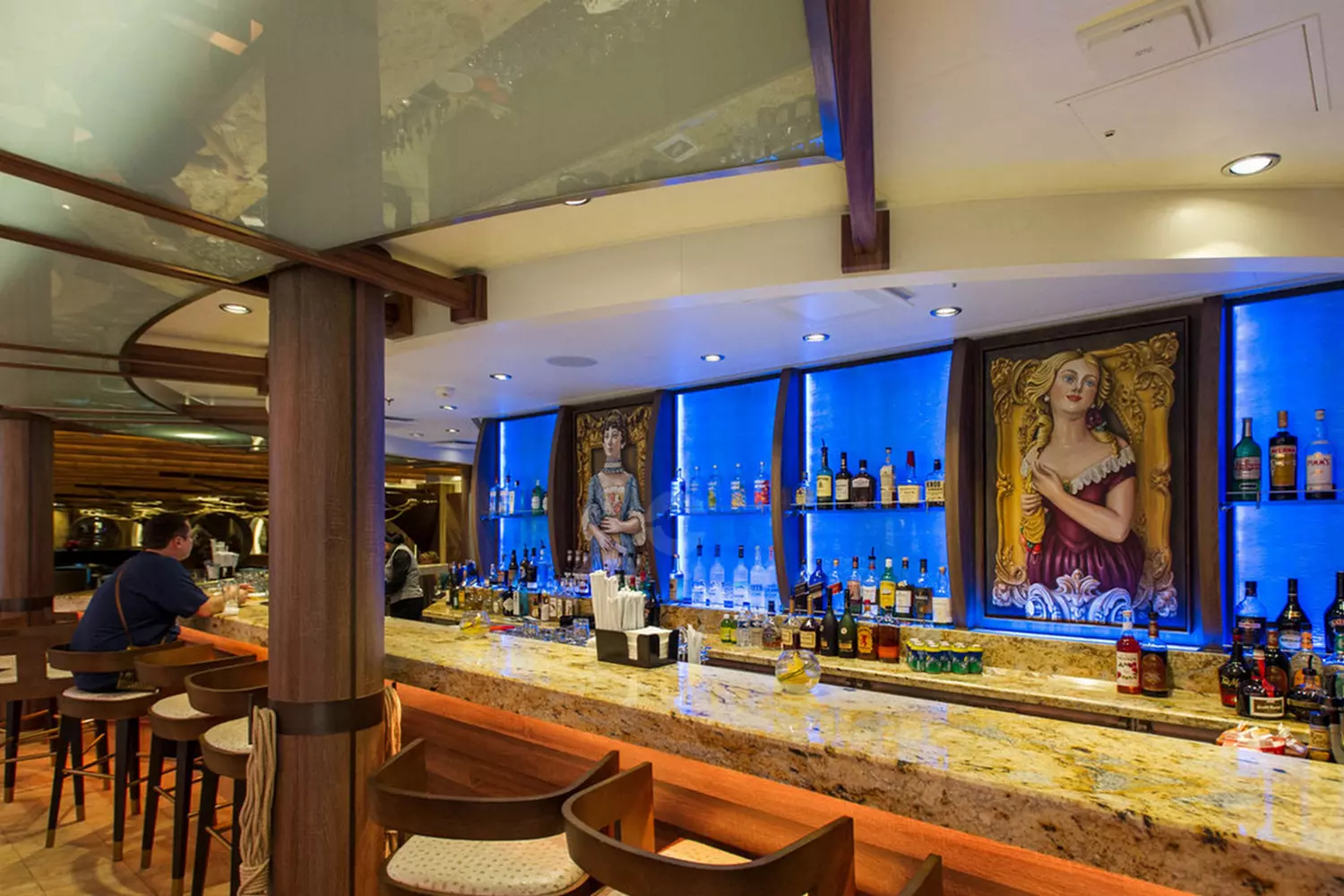 Cheers at Sea: Stylish Bars Aboard Harmony of the Seas Elegant bar area on Harmony of the Seas cruise ship with modern seating, glowing backlit shelves of premium spirits, and bartenders crafting cocktails for guests