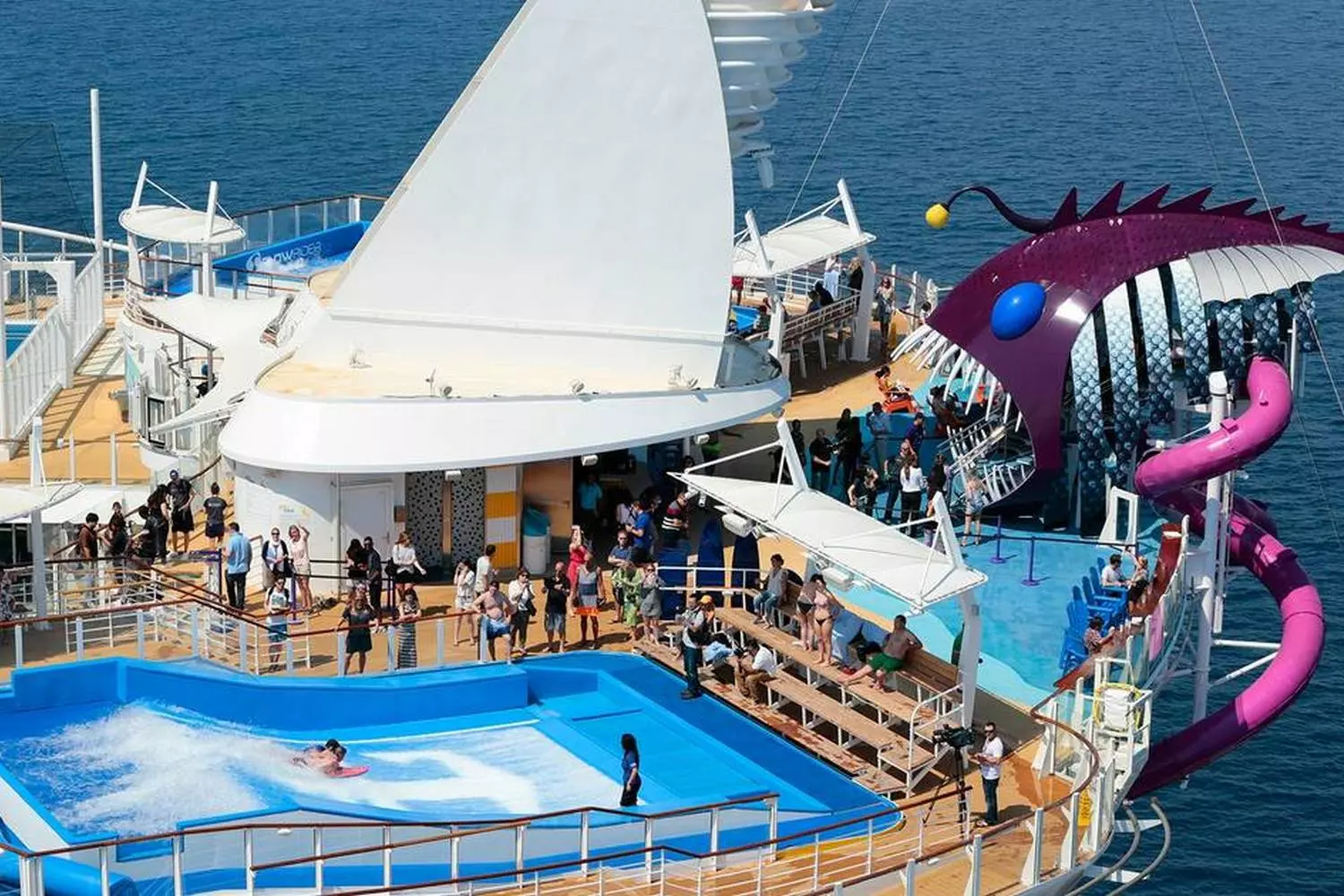 FlowRider Wave Simulator on Harmony of the Seas Excited guests riding artificial waves on Harmony of the Seas' FlowRider surf simulator, with cheering spectators and tropical deck ambiance