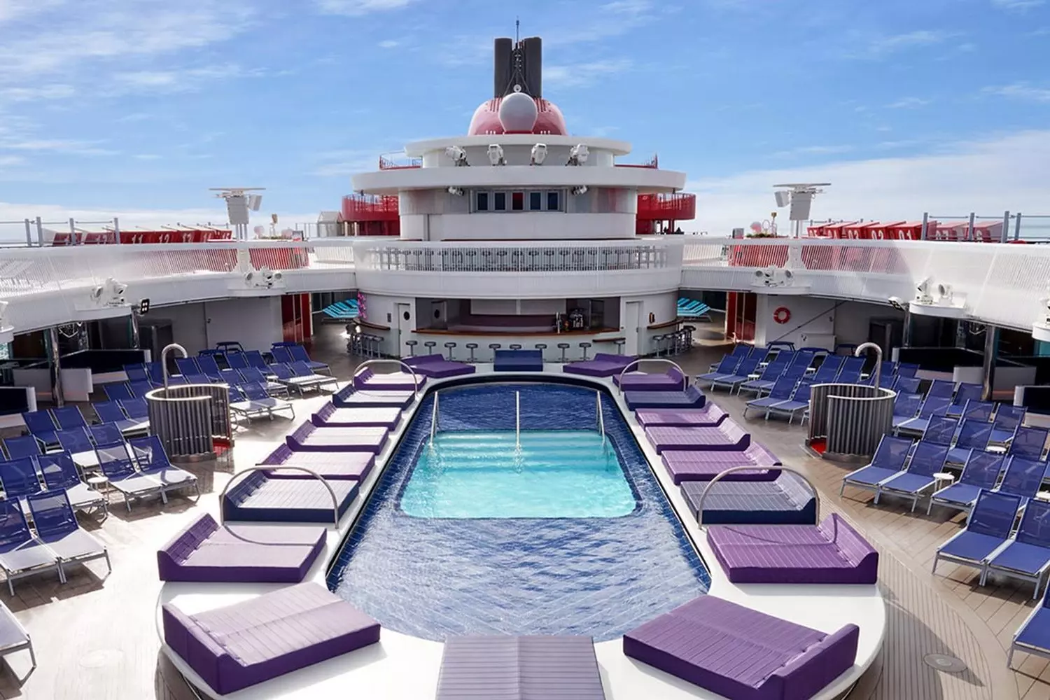 Элегантная зона у бассейна: место для релакса на Resilient Lady | Virgin Voyages Стильная зона бассейна под открытым небом на палубе лайнера Resilient Lady с шезлонгами и видом на океан