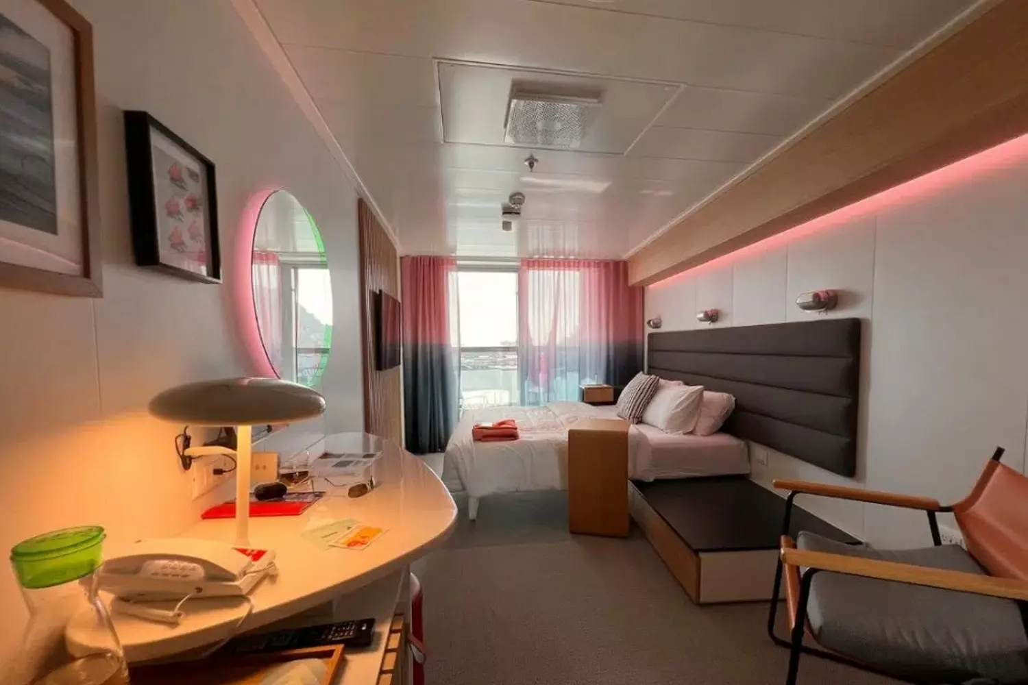 Your Sea Sanctuary: Valiant Lady's Chic Cruise Cabins | Virgin Voyages Stylish modern cabin aboard Valiant Lady cruise ship with luxury bedding, smart design and oceanview window
