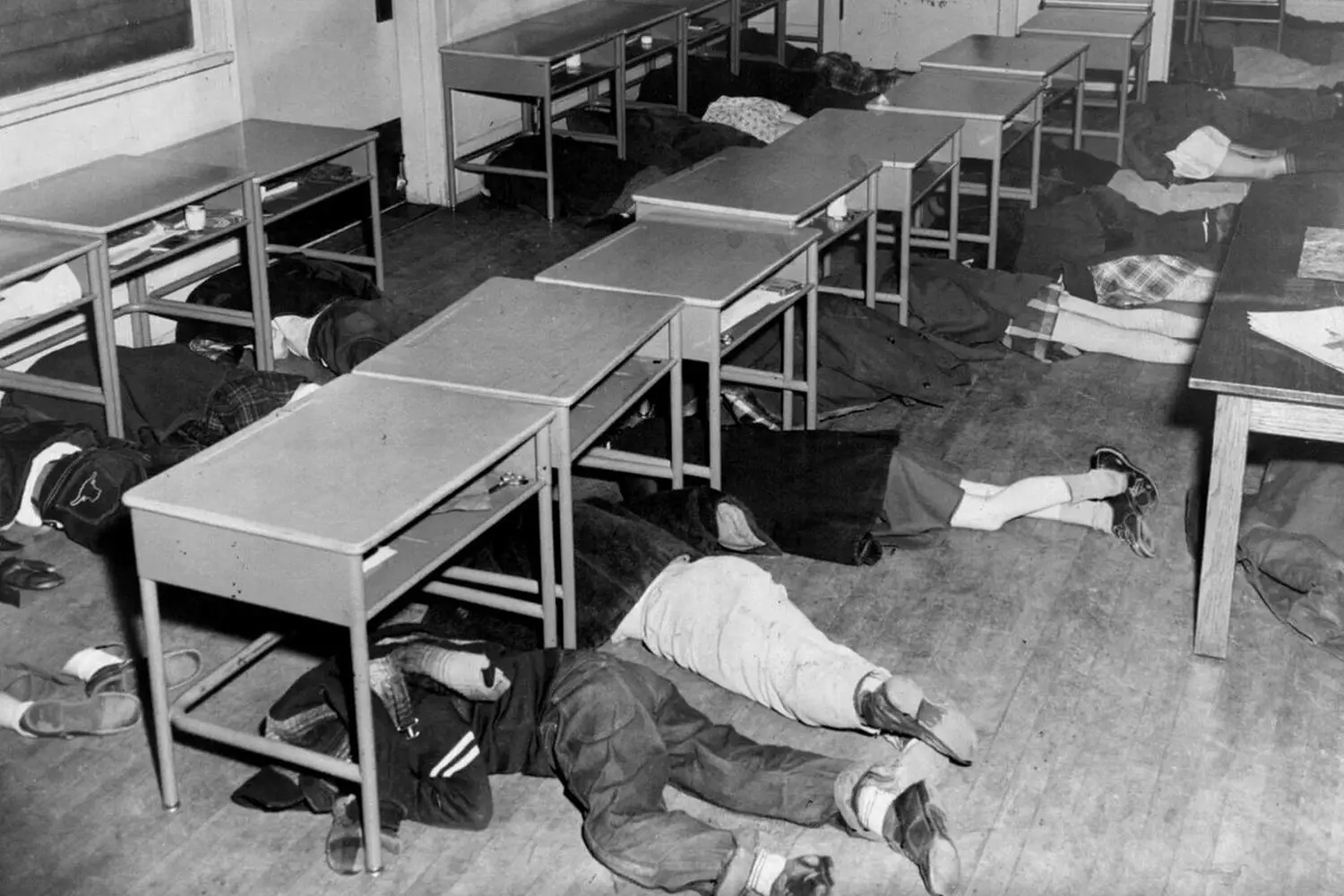 “Duck and Cover”: How American Schoolchildren Were Prepared for Nuclear War Black-and-white photo of schoolchildren in the 1950s USA hiding under desks during nuclear attack drills — part of Cold War-era propaganda