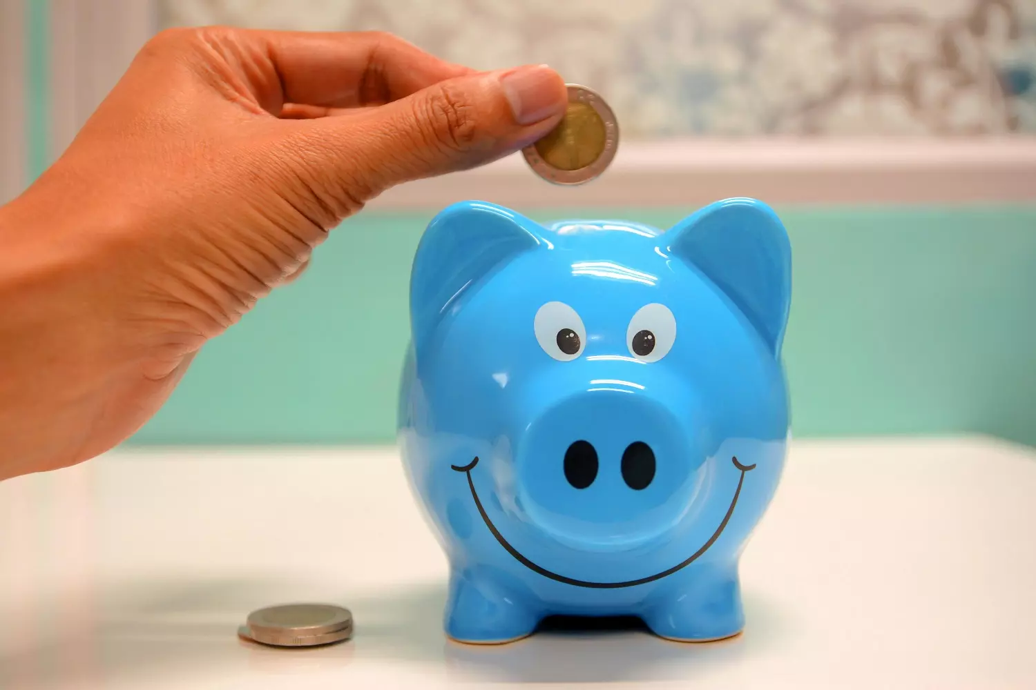 A person putting a coin into a piggy bank A person putting a coin into a piggy bank