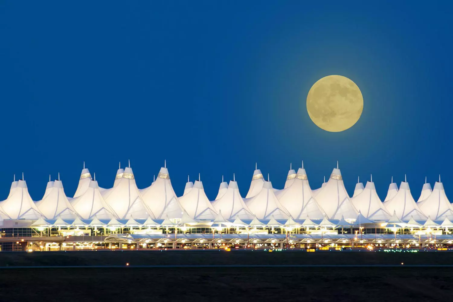 Denver Airport (DEN) — unique architecture and the largest airport in the USA by area Night view of Denver Airport with its iconic white tent-like roof and a full moon