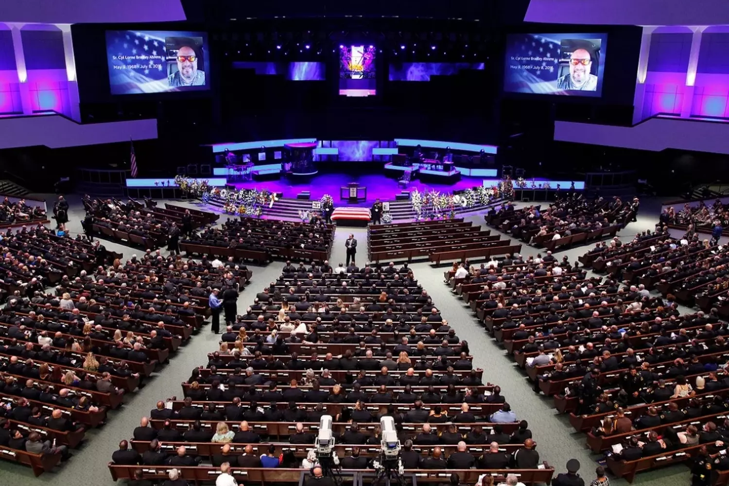 Sunday Service at a Megachurch: Faith on a Grand Scale Thousands of worshippers with raised hands at a charismatic megachurch service, with song lyrics displayed on screens and a live orchestra on stage bathed in theatrical lighting