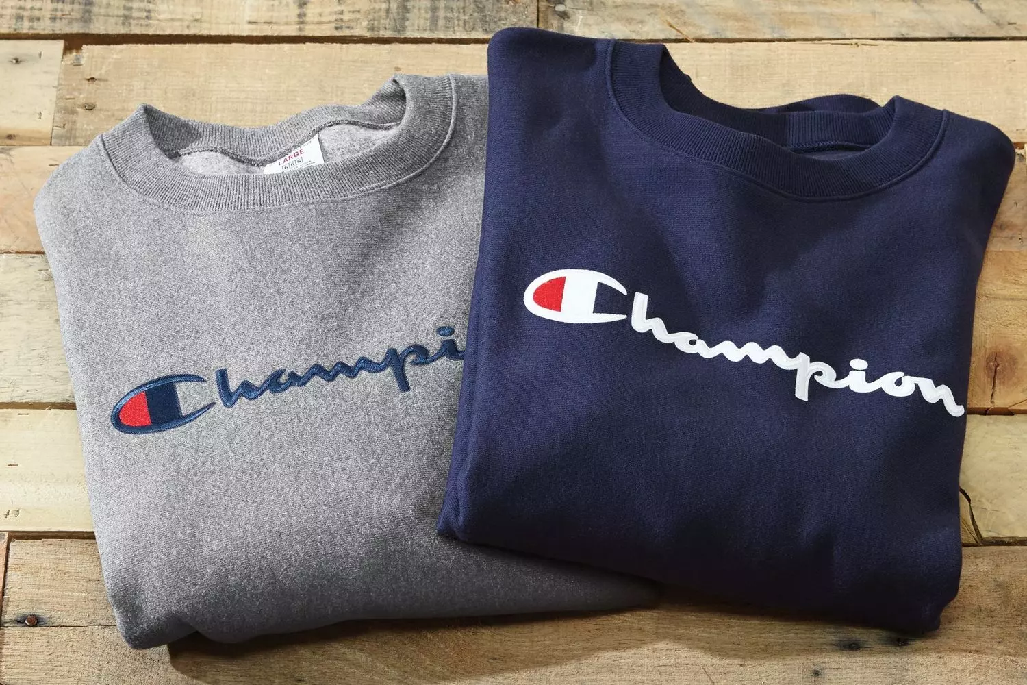 Since 1919, rewriting the hoodie rules A stack of Champion Reverse Weave sweatshirts in vintage hues: heather gray, cream, and burgundy — featuring the iconic embroidered 'C' on the sleeve, shot against a textured backdrop