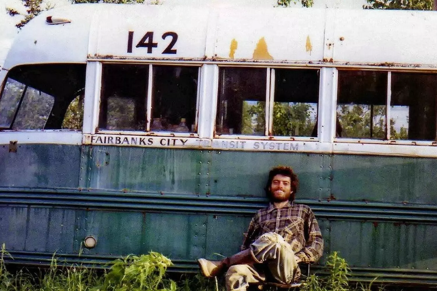Christopher McCandless at the 'Magic Bus' — A Symbol of Freedom and Tragedy (1992) Christopher McCandless, the adventurous traveler immortalized in 'Into the Wild,' standing near the abandoned bus in Alaska's wilderness with a contemplative expression