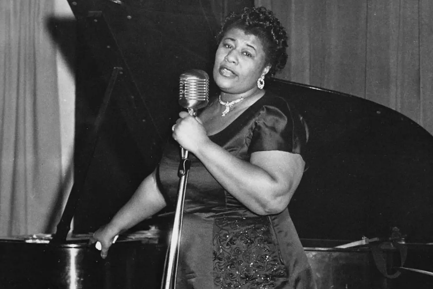 The Queen of Scat: Capturing Ella Fitzgerald’s Iconic Stage Presence Ella Fitzgerald performing on stage with a microphone, mid-song, exuding passion and energy