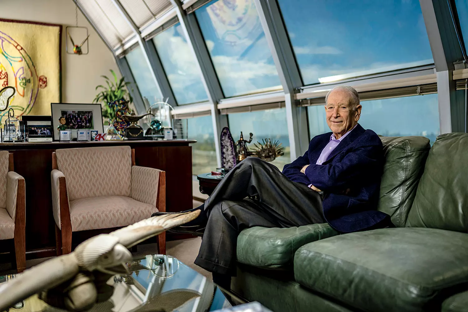 Phillip Frost – photo in the office with panoramic windows Phillip Frost in the office with a city view, sitting on a green leather sofa