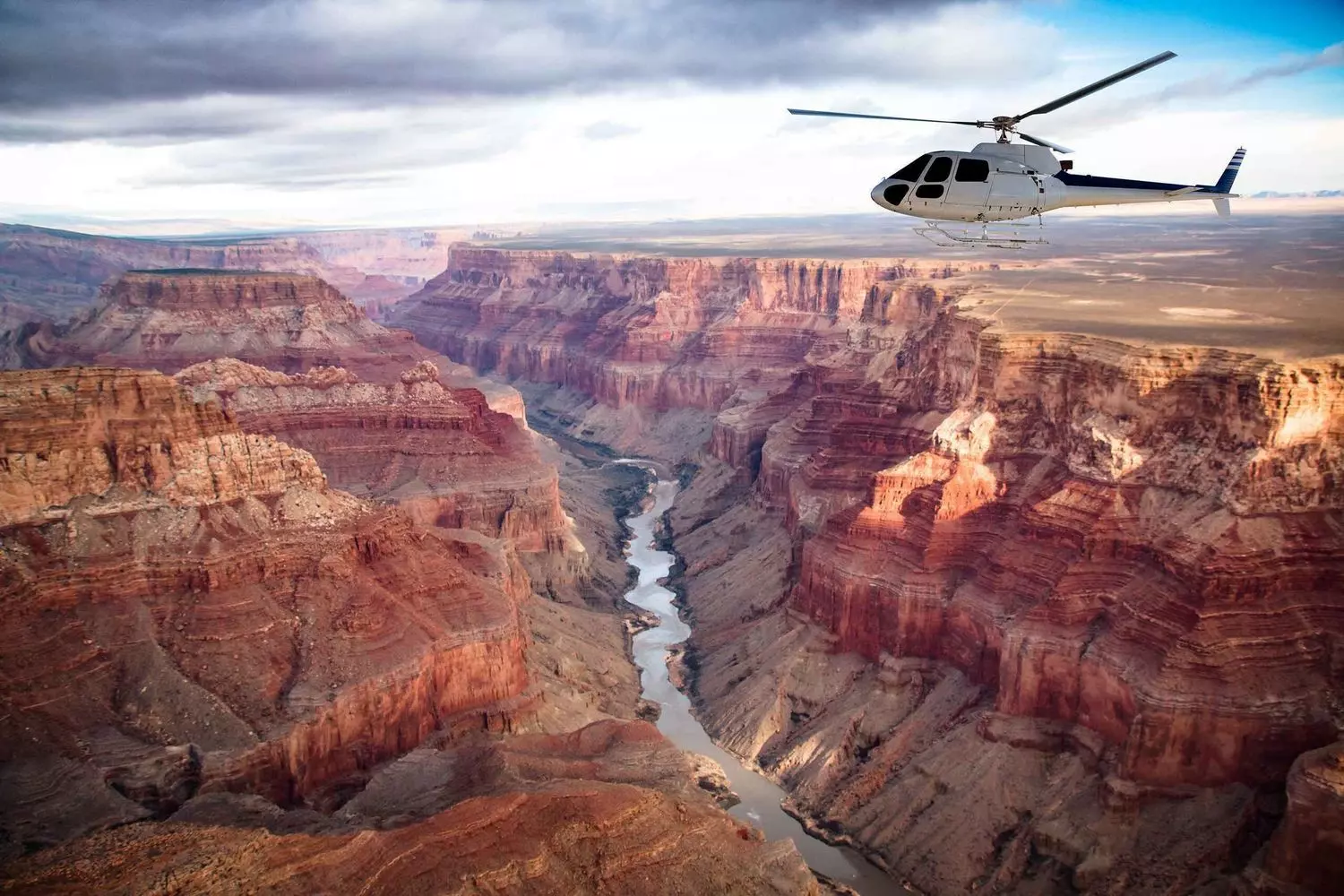 Bird's Eye Majesty: Grand Canyon Helicopter Tour Unforgettable Views Aerial view from helicopter flying over Grand Canyon showing vast red rock formations, winding Colorado River and dramatic cliffs from unique perspective