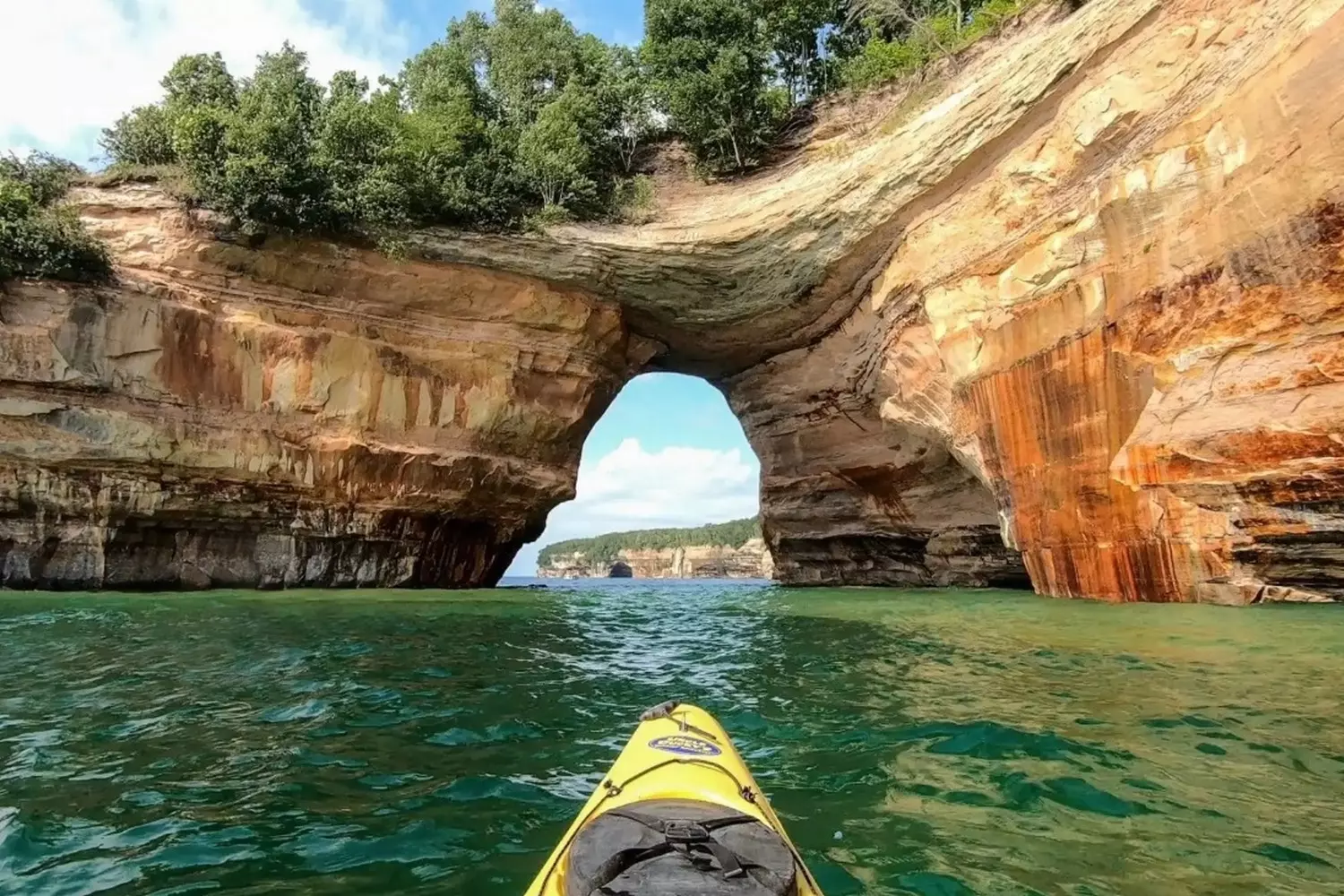 Kayaking the Great Lakes: Paddling Through Freshwater Majesty A lone kayaker glides across the crystal-clear waters of Lake Superior near Pictured Rocks, with towering sandstone cliffs reflecting in the calm surface