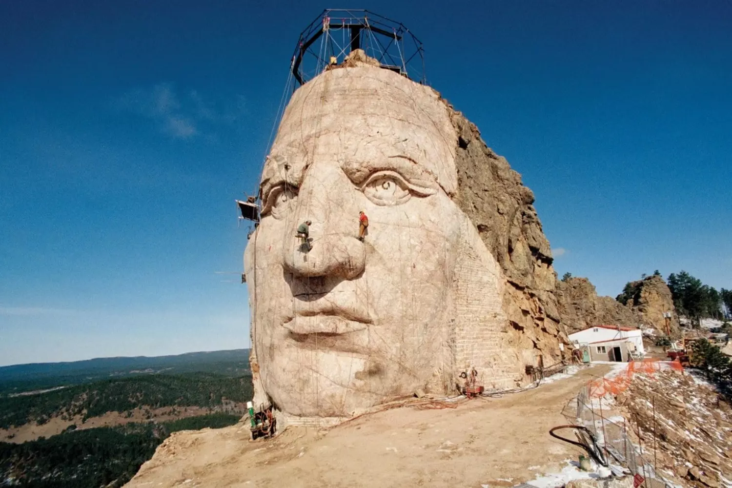 Crazy Horse Memorial: The World's Largest Mountain Carving in Progress Partial face of Crazy Horse emerging from Thunderhead Mountain with construction equipment visible, showcasing the ongoing monumental carving project in South Dakota